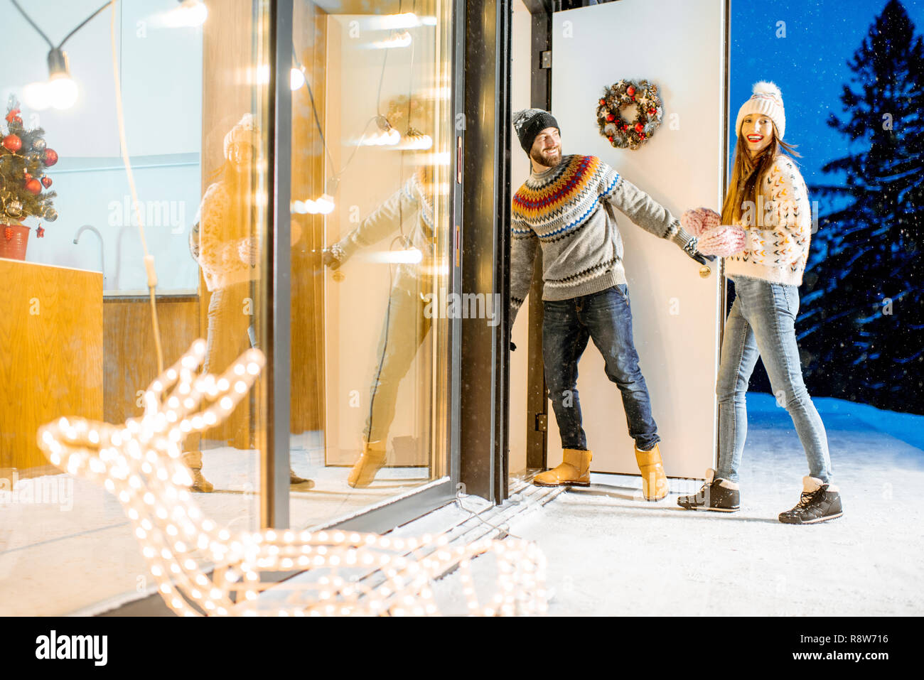 Jeune couple venant dans la magnifique maison décorée durnig les vacances d'hiver dans les montagnes enneigées Banque D'Images