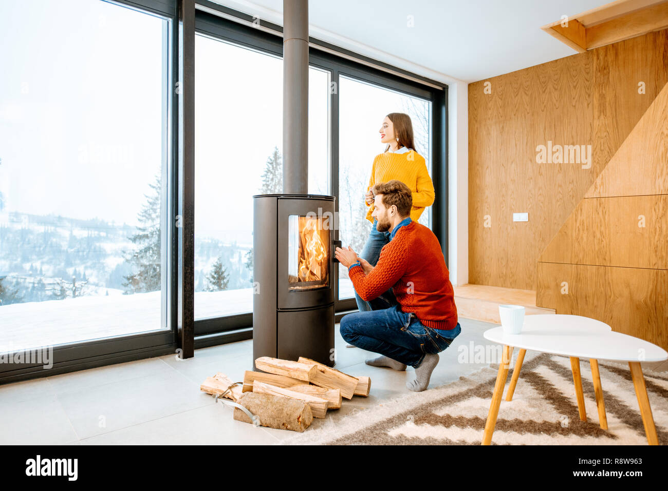 Jeune couple vêtus de chandails lumineux réchauffe près de la cheminée dans la maison moderne dans les montagnes pendant l'hiver Banque D'Images