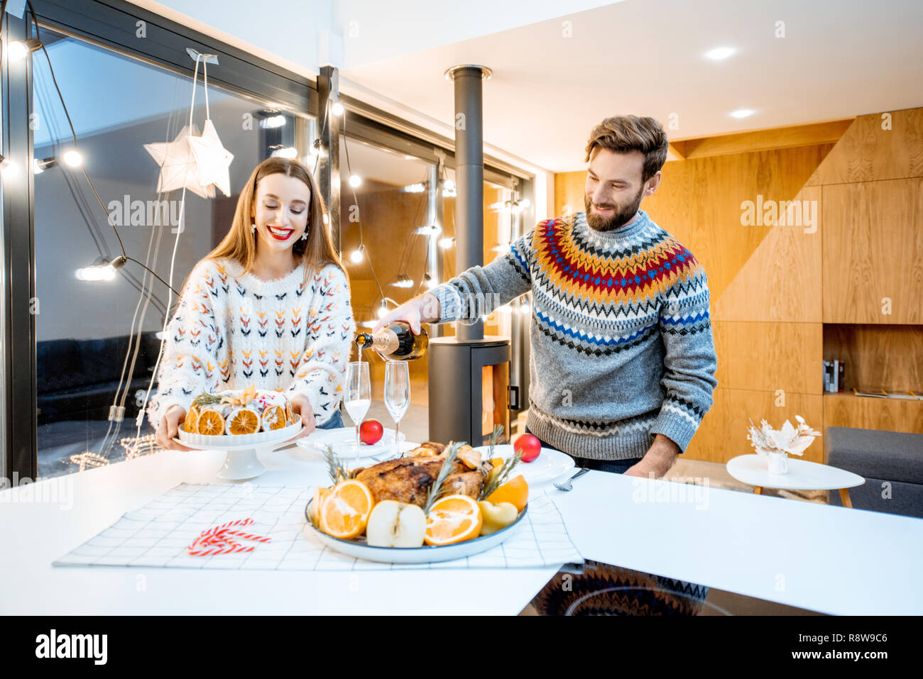 Jeune couple ayant dîner de fête assis ensemble dans la maison moderne durant les vacances d'hiver Banque D'Images