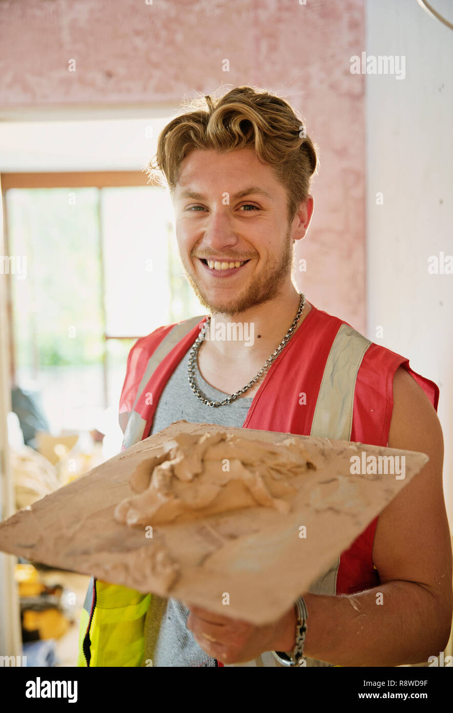 Portrait souriant, confiant young construction worker plastering Banque D'Images