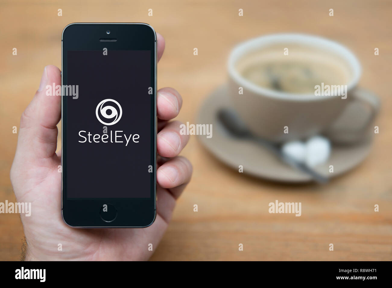 Un homme se penche sur son iPhone qui affiche le logo SteelEye (usage éditorial uniquement). Banque D'Images