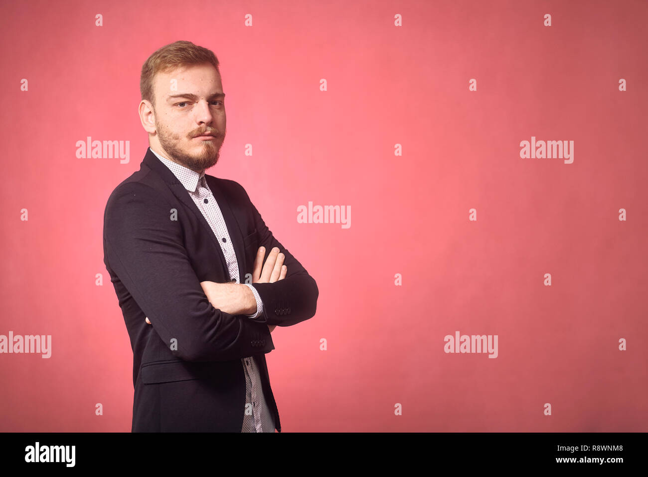 Un jeune homme, 29 ans, sérieux, les bras croisés, à la recherche d'appareil photo. pink background, studio shot, séance photo. Banque D'Images