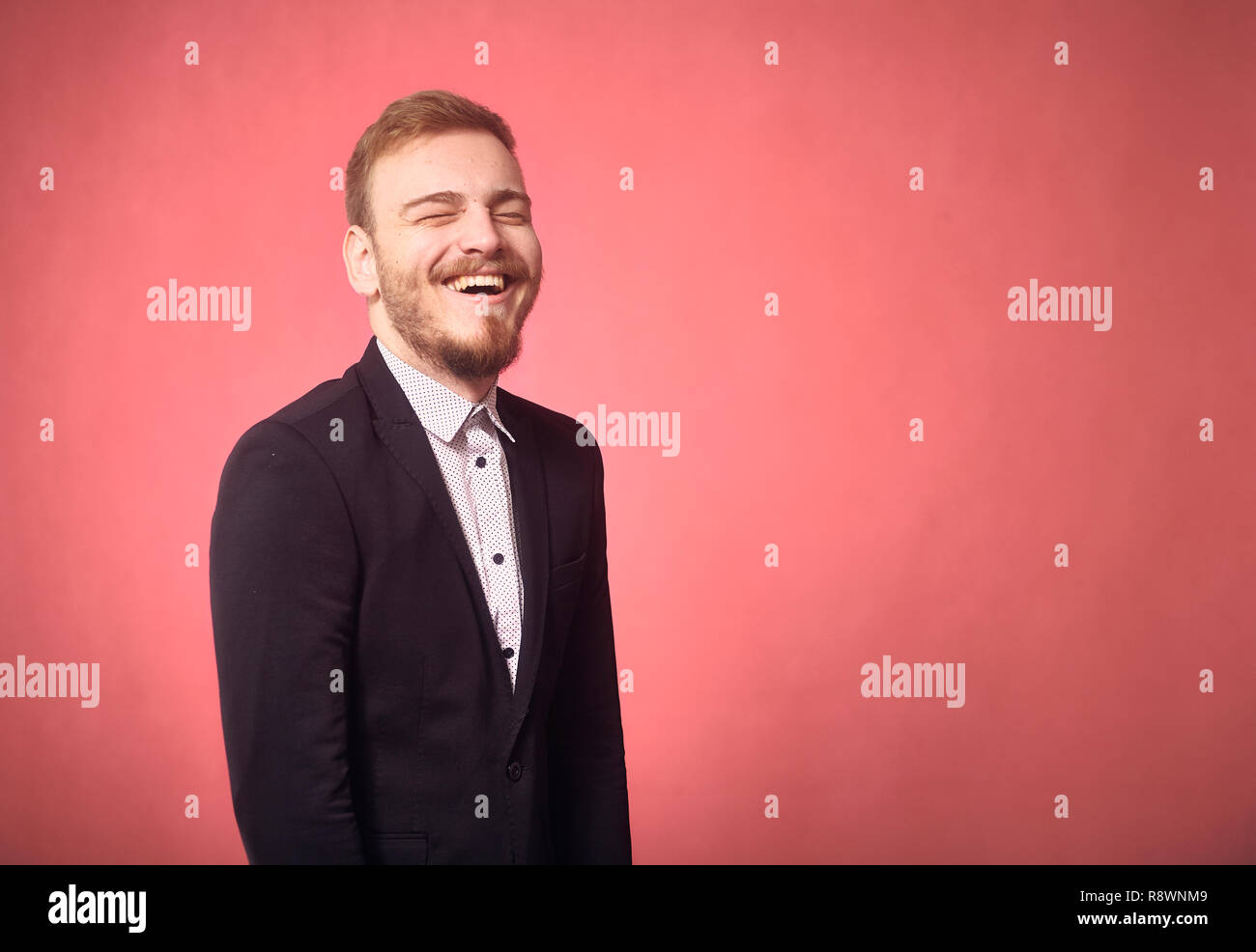 Un jeune homme, 29 ans, drôle d'expression, le rire franc, les yeux fermés. pink background, studio shot, séance photo. Banque D'Images