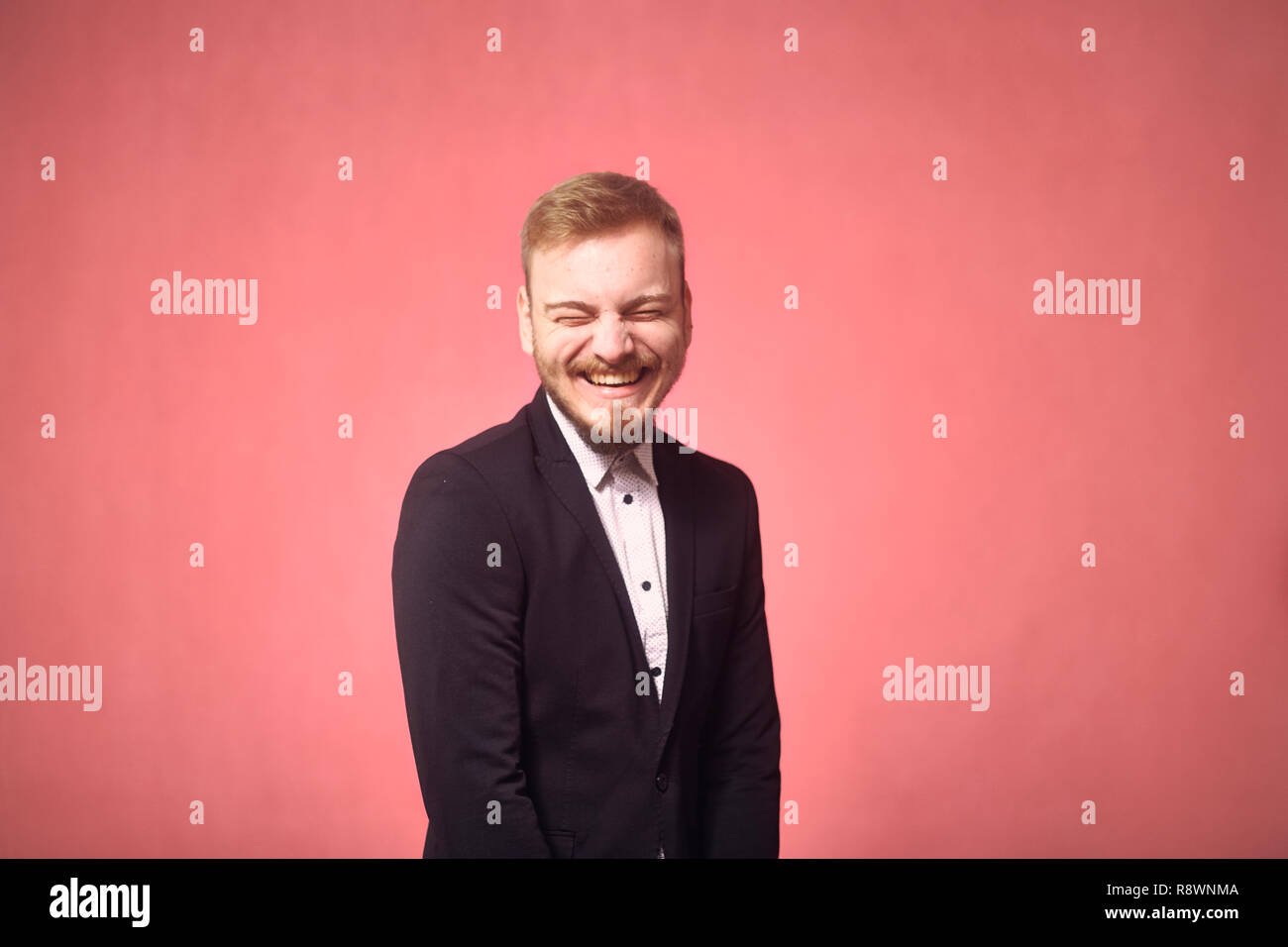 Un jeune homme, 29 ans, drôle d'expression, le rire franc, les yeux fermés. pink background, studio shot, séance photo. Banque D'Images
