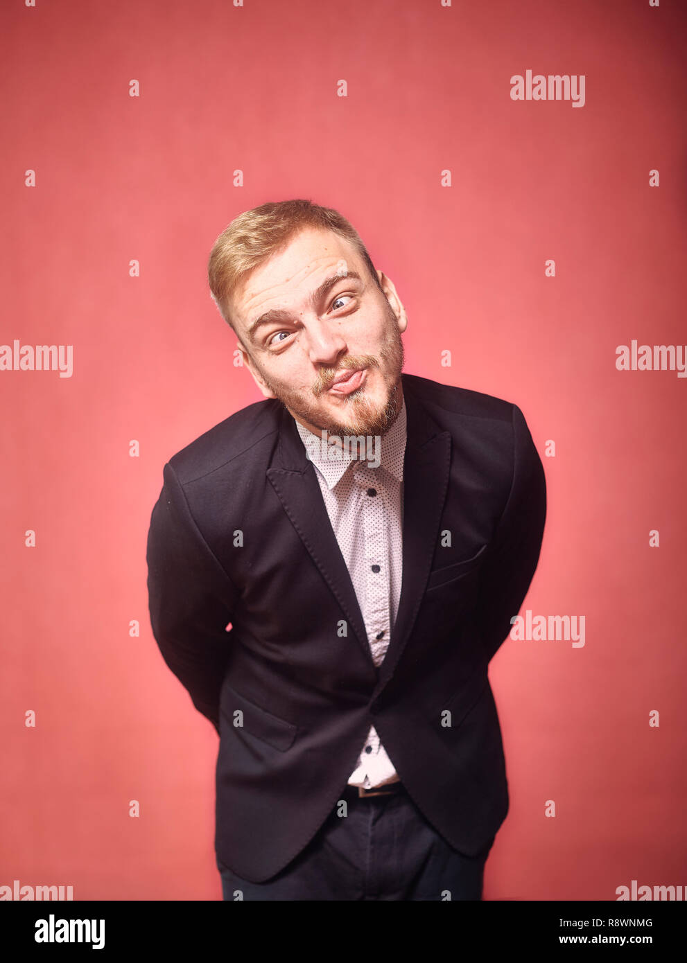 Un jeune homme, 29 ans, ce qui pose, drôle d'expression, se penchant en avant. pink background, studio shot, séance photo. Banque D'Images