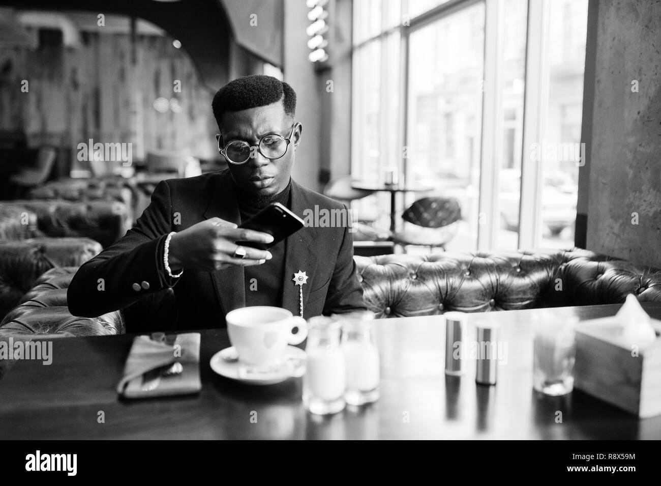 La mode african american man in suit et verres assis au café et le café sur téléphone. Banque D'Images