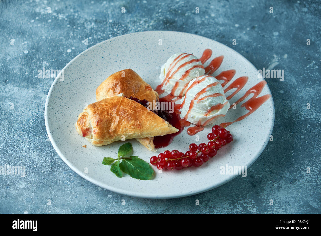 Des tranchées d'un strudel aux fruits rouges frais servi avec des baies de cassis et le sucre en poudre sur une vieille base sur une assiette avec de la crème glacée Banque D'Images