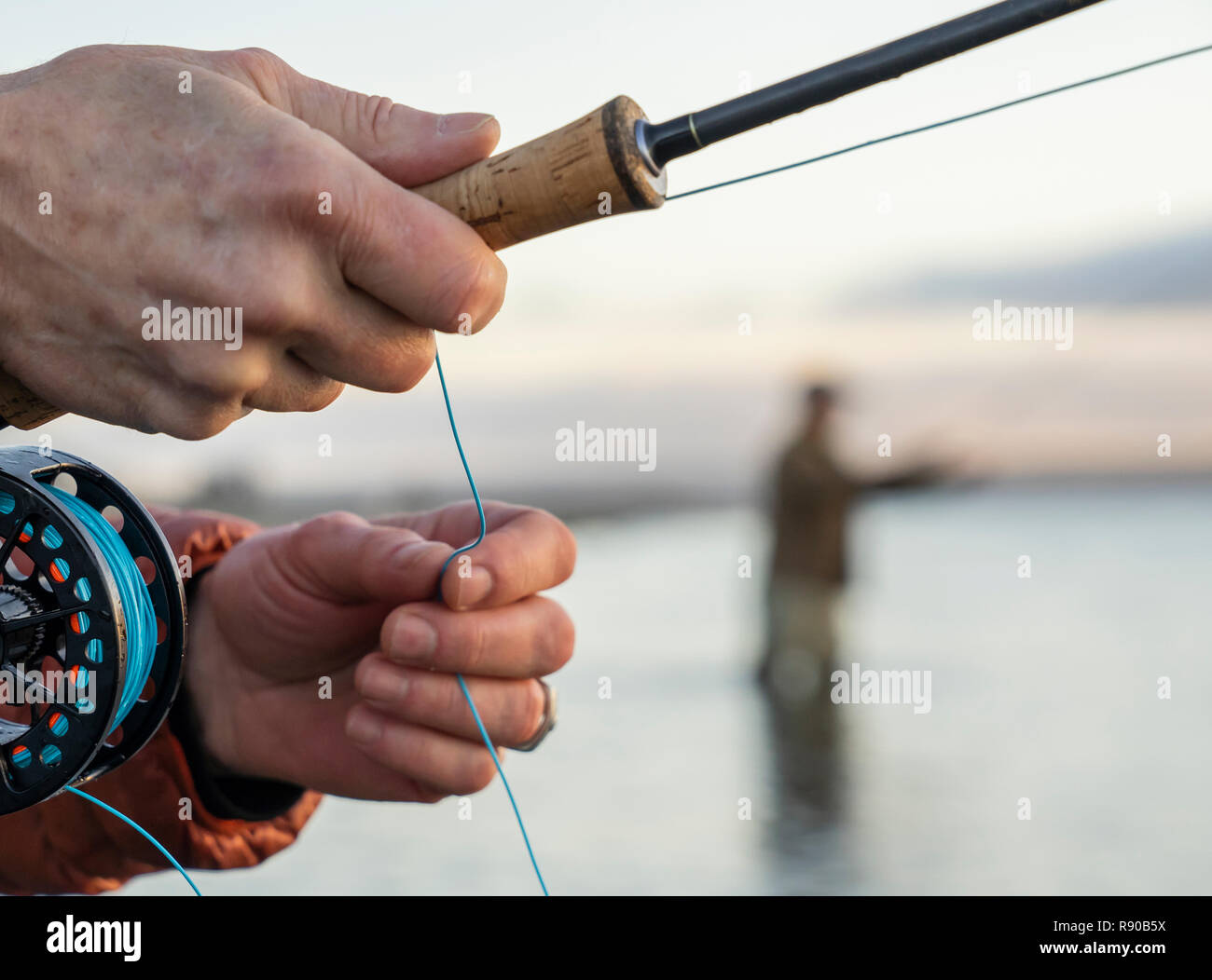 Un gros plan d'un fly fisherman's hands holding sa canne à mouche et de ligne pendant la pêche. Banque D'Images