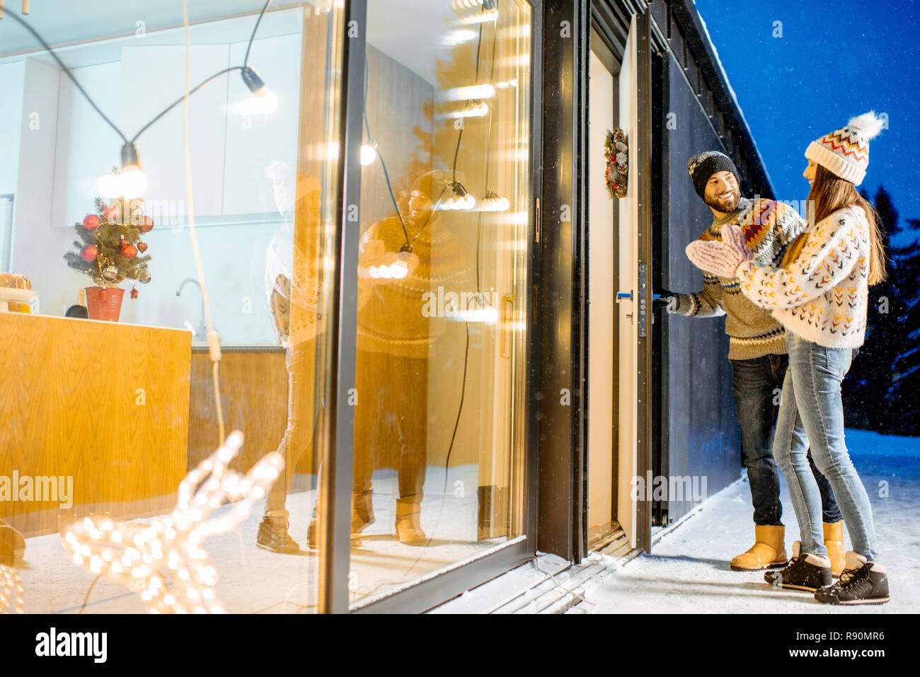 Jeune couple venant dans la magnifique maison décorée durnig les vacances d'hiver dans les montagnes enneigées Banque D'Images