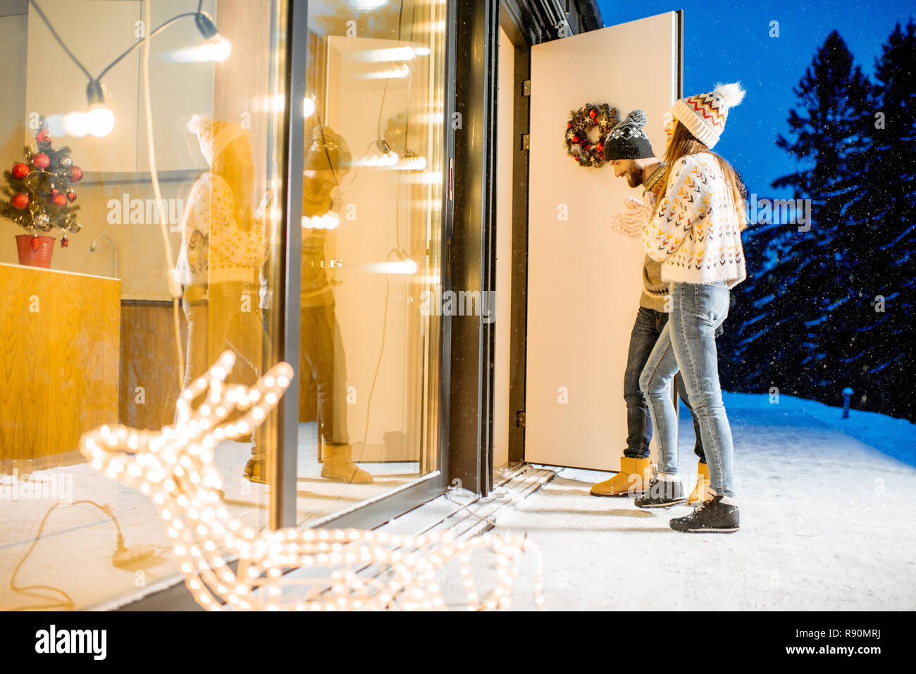 Jeune couple venant dans la magnifique maison décorée durnig les vacances d'hiver dans les montagnes enneigées Banque D'Images