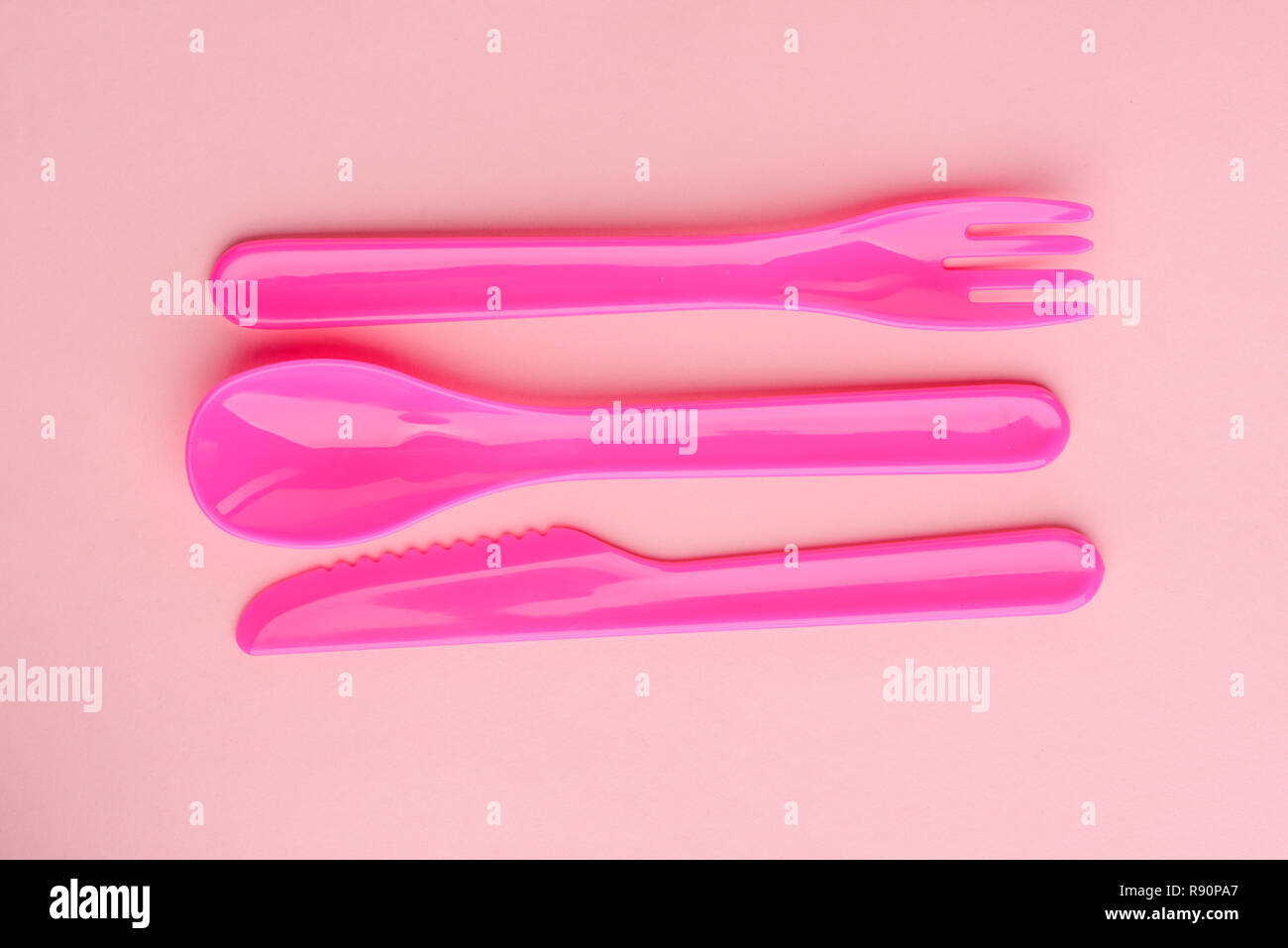 Couverts en plastique lumineux situé sur fond rose. Couteau mignon, cuillère et fourchette pour les jeux des enfants. Banque D'Images