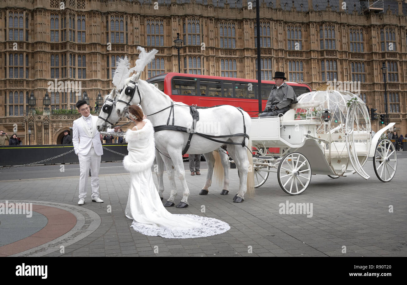 Couple mariés chinois habillé en blanc de poser pour les photos de mariage de conte de fées, avec chariot blanc tiré par deux chevaux blancs, à l'extérieur du parlement, Londres. Banque D'Images