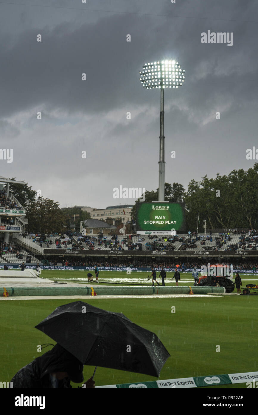 De fortes pluies au cours d'un test match à Lords. Les projecteurs de couleurs vives en colère contre un blaze ciel gris. Au premier plan un spectateur s'exécute pour couvrir Banque D'Images