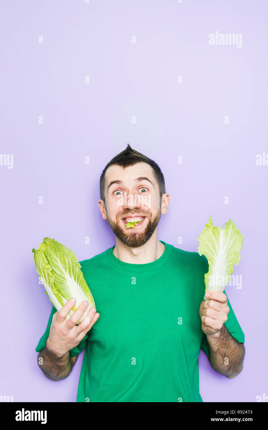 Jeune homme mordre sur une feuille de chou nappa, Beijing face plaisir d'expression. Fond mauve, copiez l'espace, orientation verticale. Banque D'Images