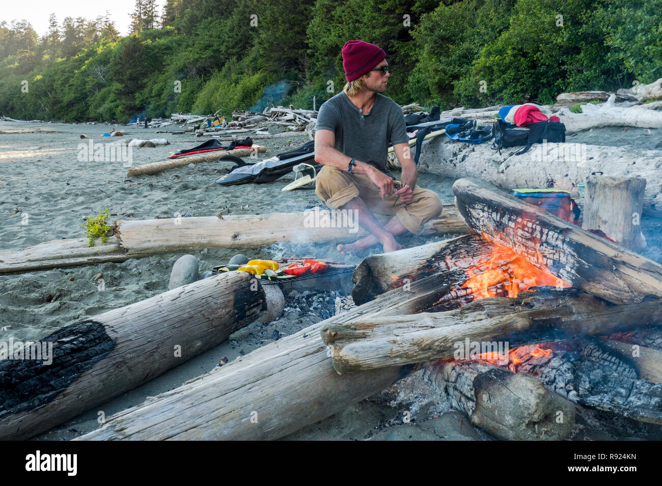 Un homme est assis par un incendie et attend pour apprécier un barbecue après une session de surf à la baie Florencia dans Tofion, British Columbia, Canada Banque D'Images