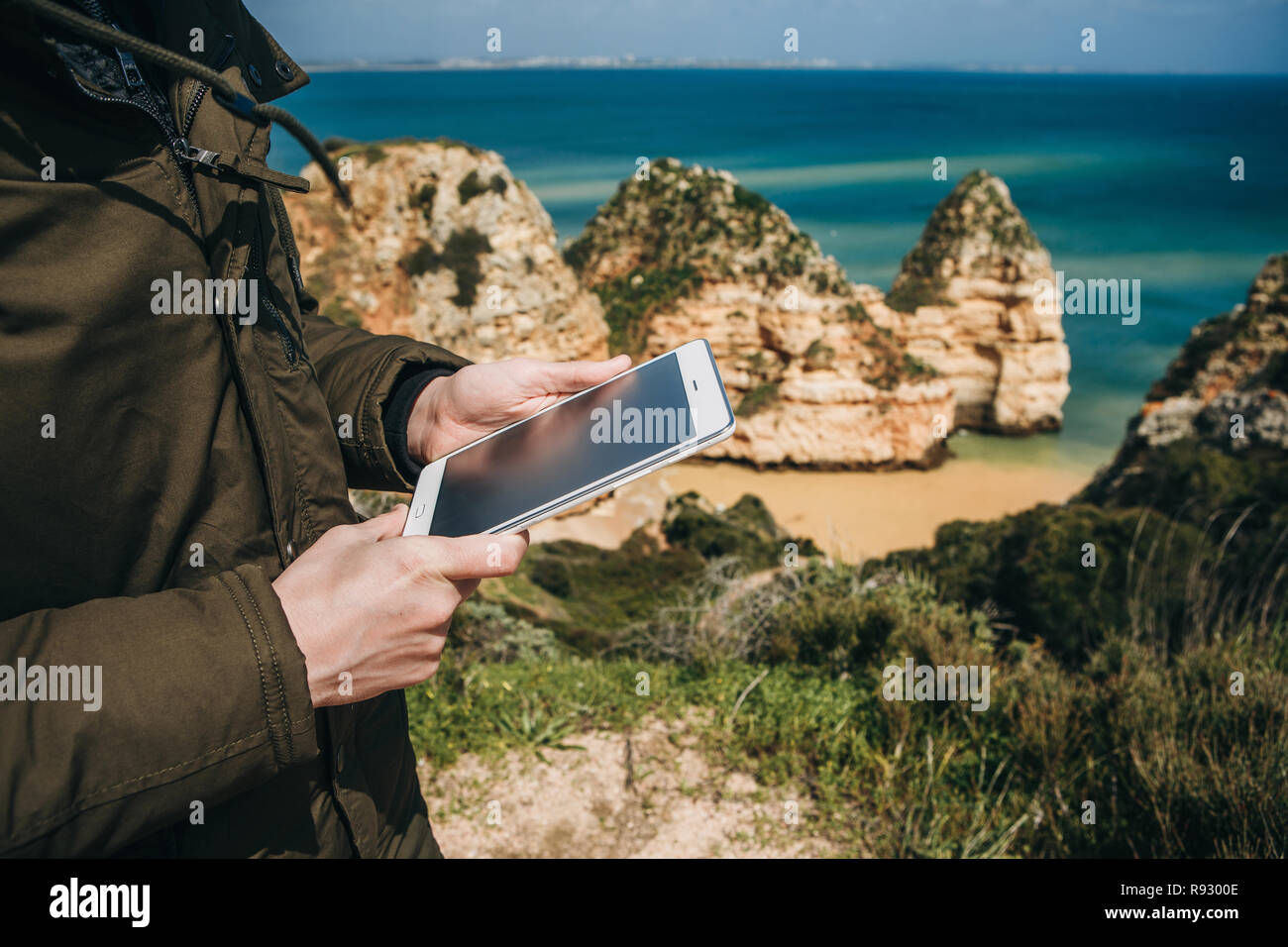 Close-up. Un touriste ou voyageur utilise une tablette pour afficher une carte ou une autre application mobile. L'Océan atlantique près de la ville de Lagos au Portugal dans l'arrière-plan. Banque D'Images