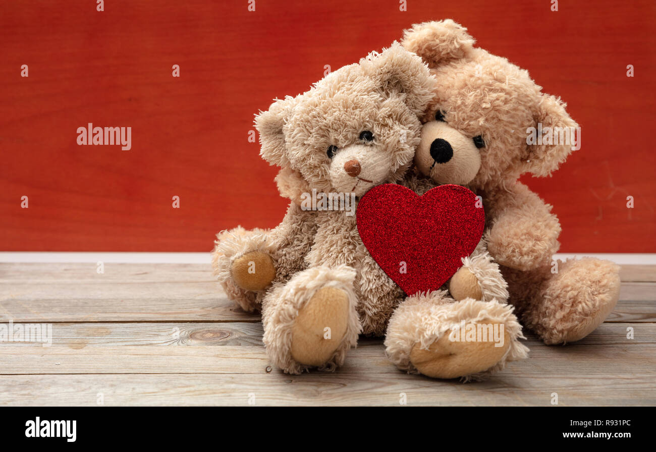 L'amour, l'amitié concept, bras. Deux ours en embrassant comme un couple sur un plancher en bois, red wall background, copiez l'espace. Banque D'Images