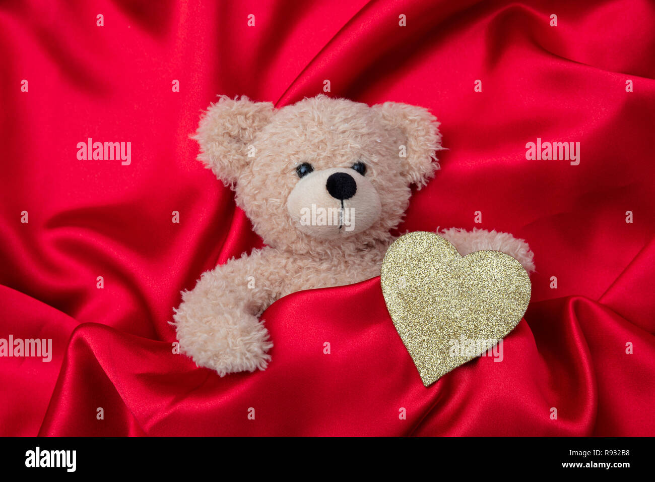 Valentines Day. Vue de dessus de l'ours en peluche et coeur en or sur fond de soie rouge, papier peint. Banque D'Images