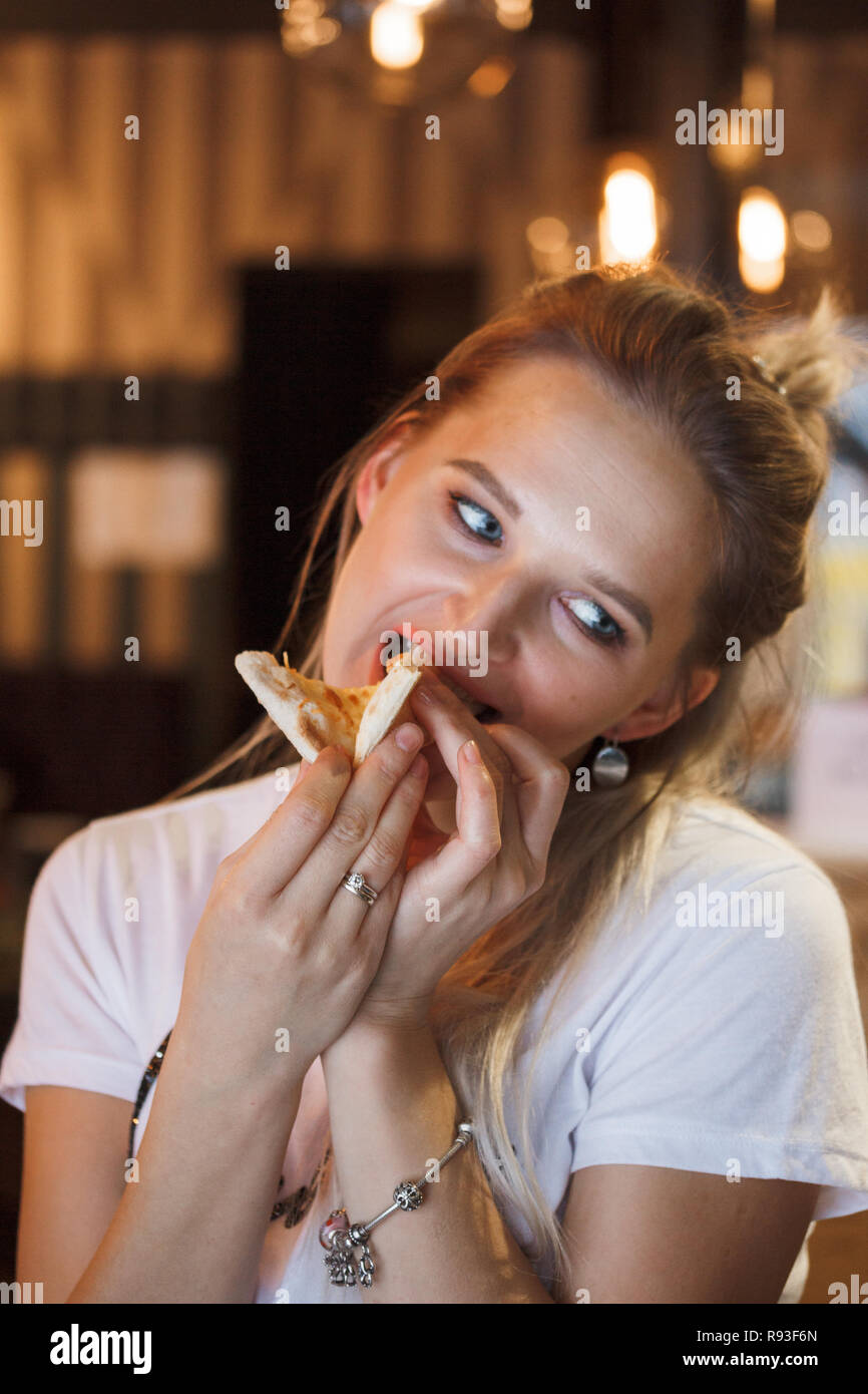 Casual girl eating pizza dans le restaurant et profiter de ce. Funny blonde girl in white t-shirt eating pizza au restaurant Banque D'Images