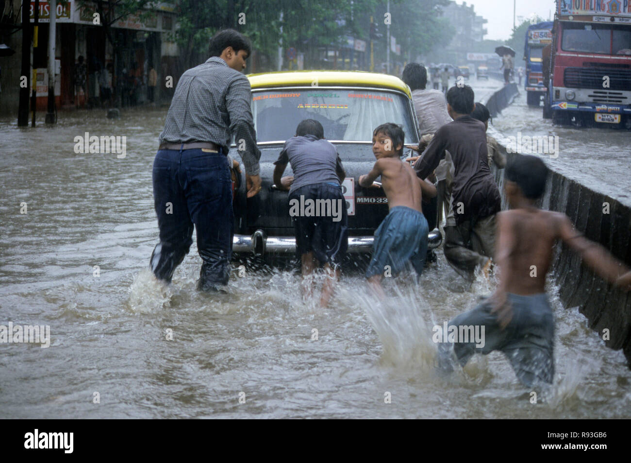 En raison de fortes pluies des inondations, les enfants poussant Taxi sur La route inondée, Bombay Mumbai, Maharashtra, Inde Banque D'Images