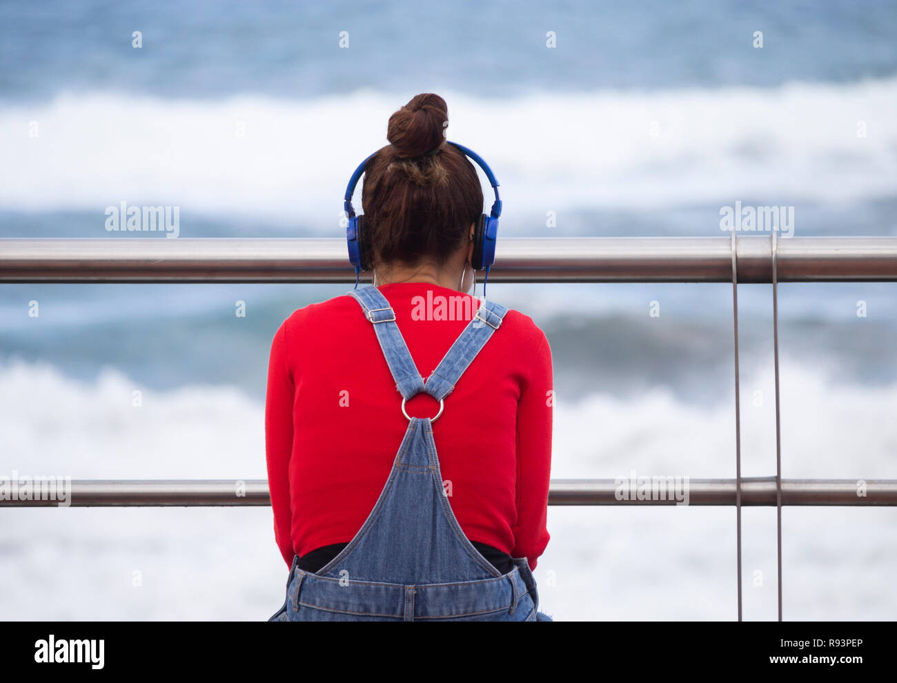 Vue arrière du jeune femme portant des écouteurs assis sur son fauteuil avec vue sur la mer. Banque D'Images