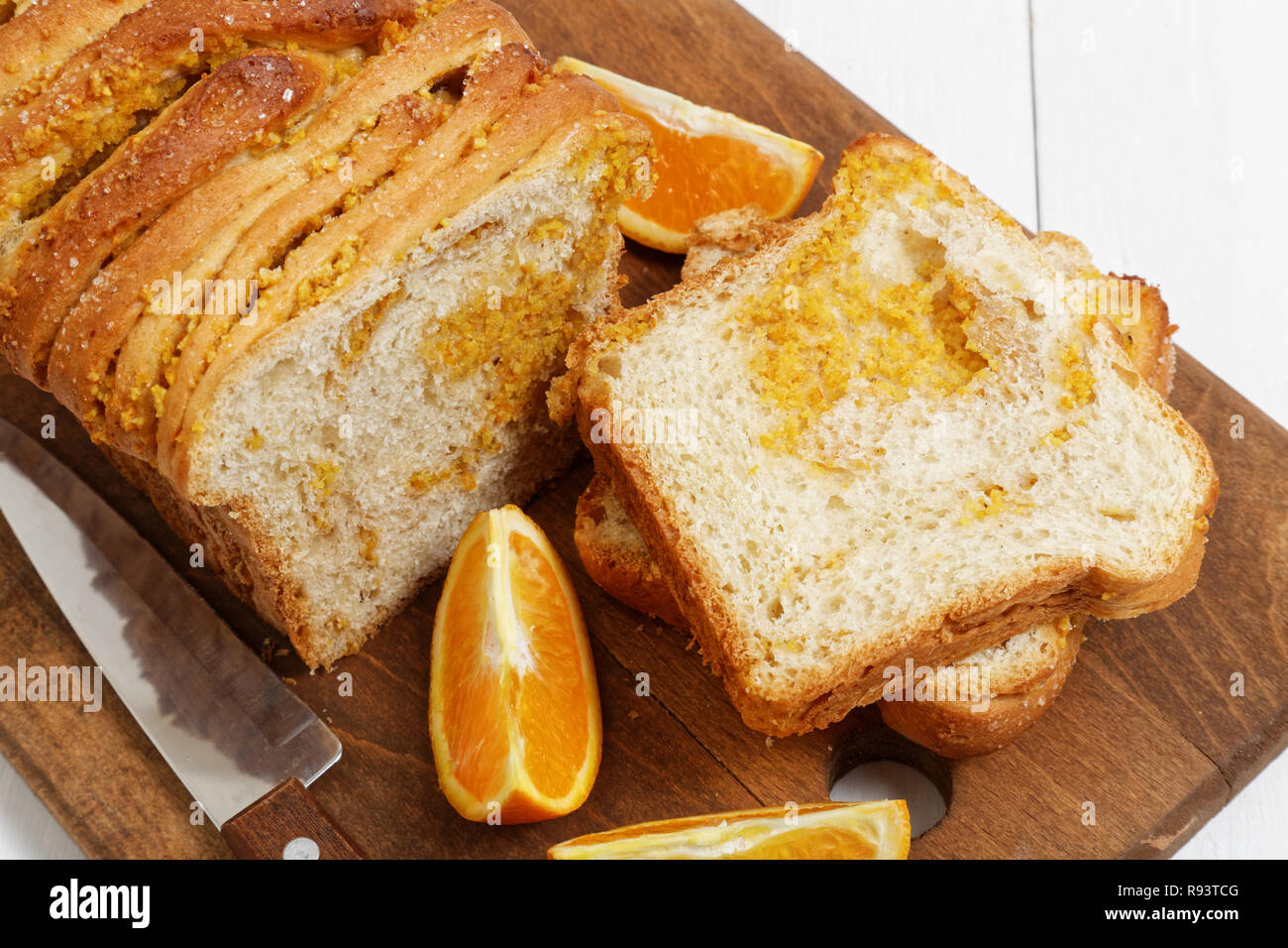 Libre du pain avec le zeste d'orange et les noix sur la table en bois blanc. Près d'un couteau et des tranches d'oranges fraîches. Banque D'Images