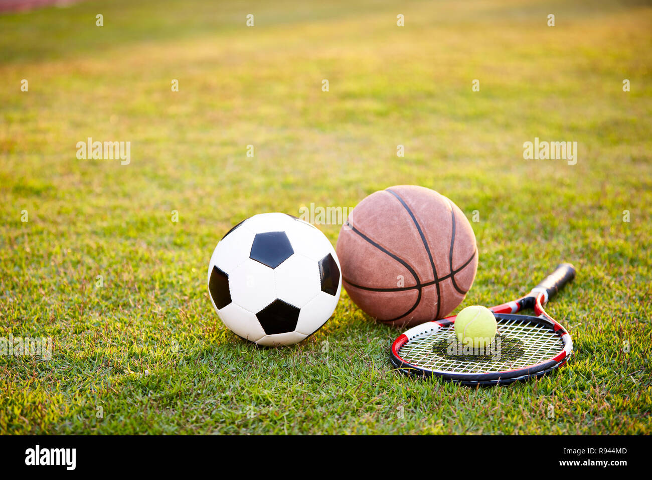 Ballon de soccer de football basket-ball tennis racket portées sur l'herbe au coucher du soleil Banque D'Images