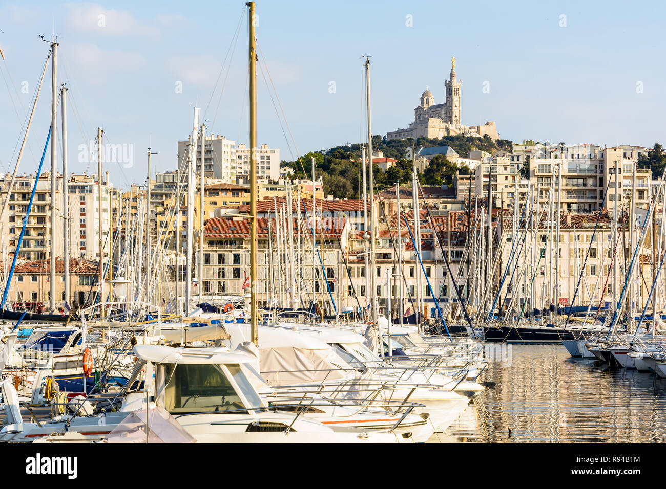 Les bateaux de plaisance amarrés dans le port de plaisance du Vieux Port de Marseille, France, avec la basilique Notre-Dame de la garde en haut de la colline au coucher du soleil. Banque D'Images