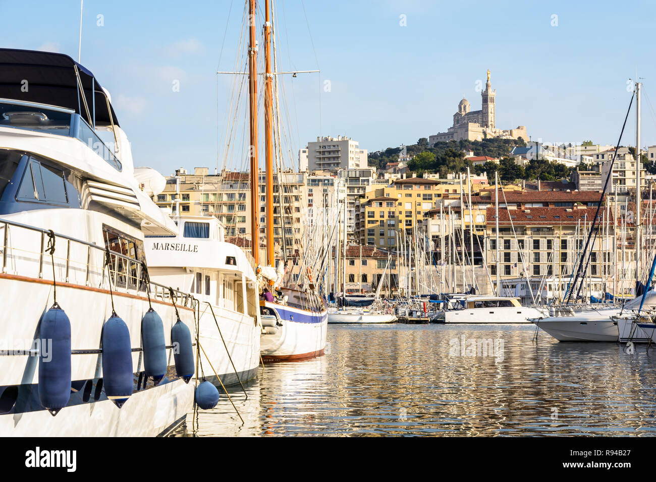 Yachts et voiliers amarrés dans le Vieux Port de Marseille, France, avec la basilique Notre-Dame de la garde en haut de la colline au coucher du soleil. Banque D'Images