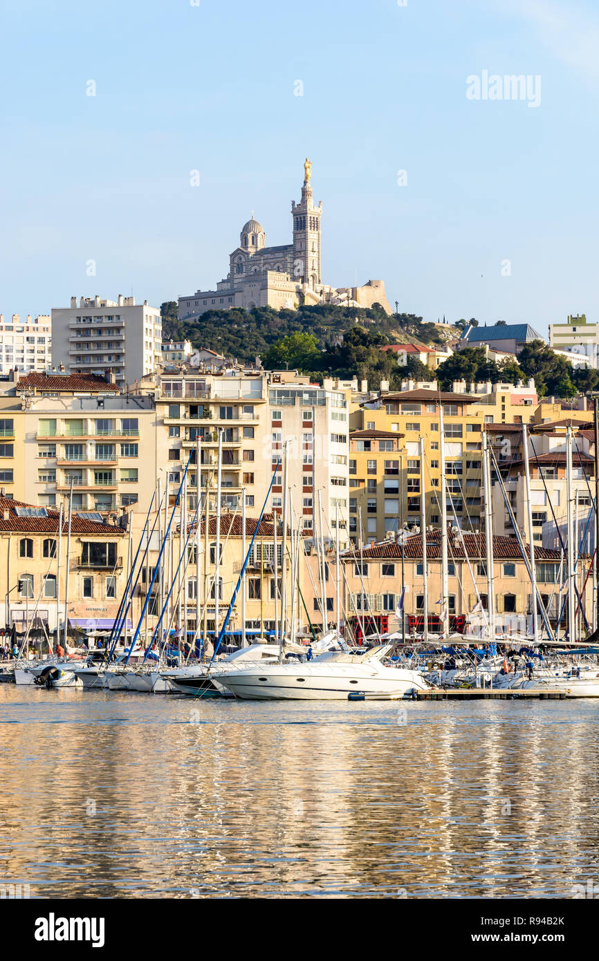 Le Vieux Port de Marseille, France, avec les bateaux et voiliers amarrés dans le port de plaisance et la basilique Notre-Dame de la garde en haut de la colline au coucher du soleil Banque D'Images