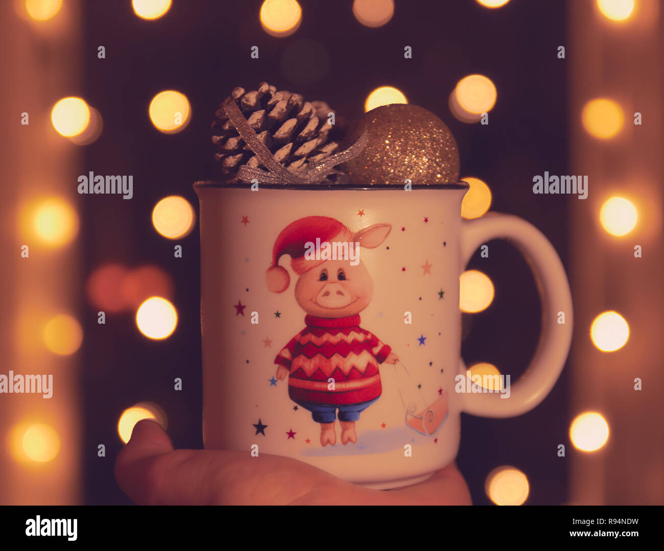 Thème de Noël. dans la main d'un mug avec un cochon et des boules de Noël. bokeh en arrière-plan. Lumières scintillantes. Banque D'Images