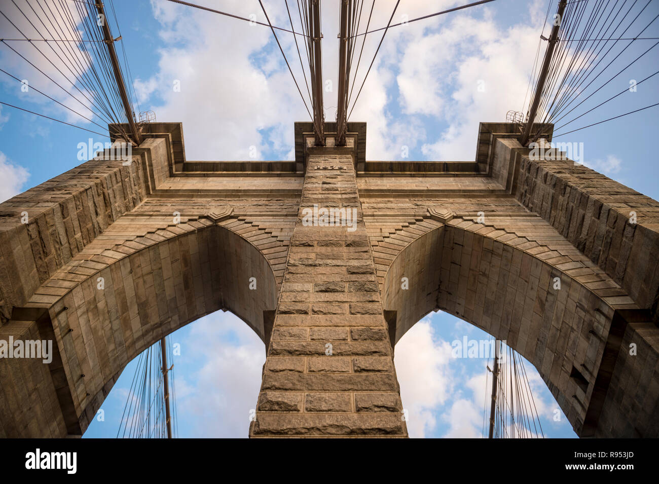 Scenic abstraite de câbles d'acier et les briques texturée de l'emblématique tour à voûte en pierre du pont de Brooklyn sous soleil nuages doux Banque D'Images