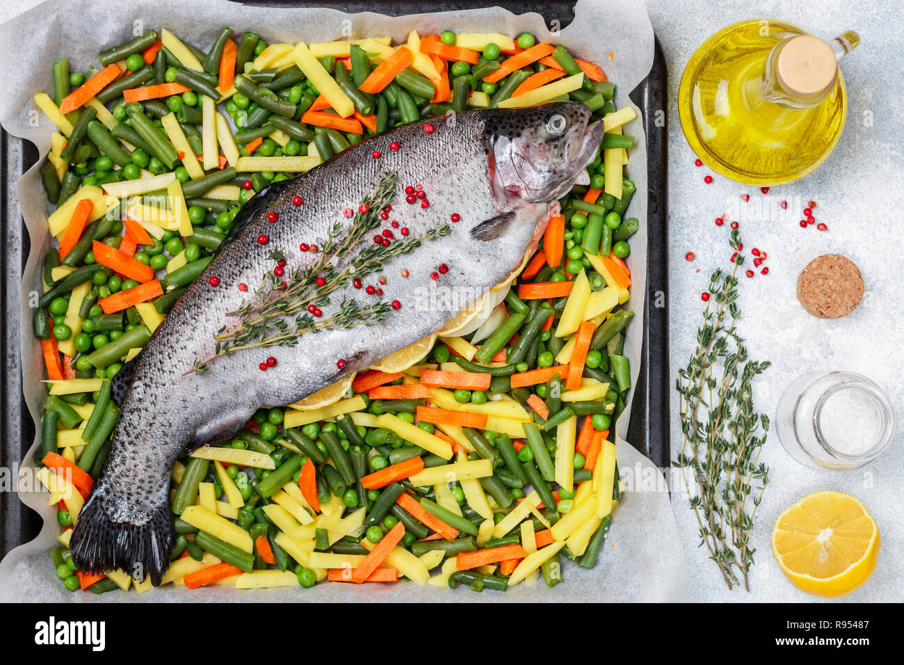 La truite poisson cru avec des légumes (pommes de terre, carottes, haricots, petits pois et oignons) est prêt pour la cuisson avec le citron, le thym et le poivre rose. Sa sauvage Banque D'Images