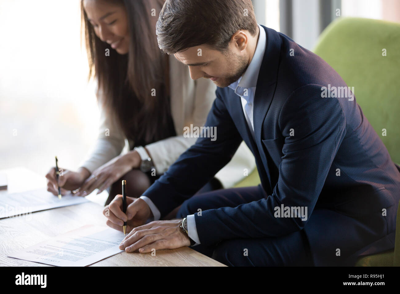 Asian and Caucasian woman sitting at desk signature contr Banque D'Images