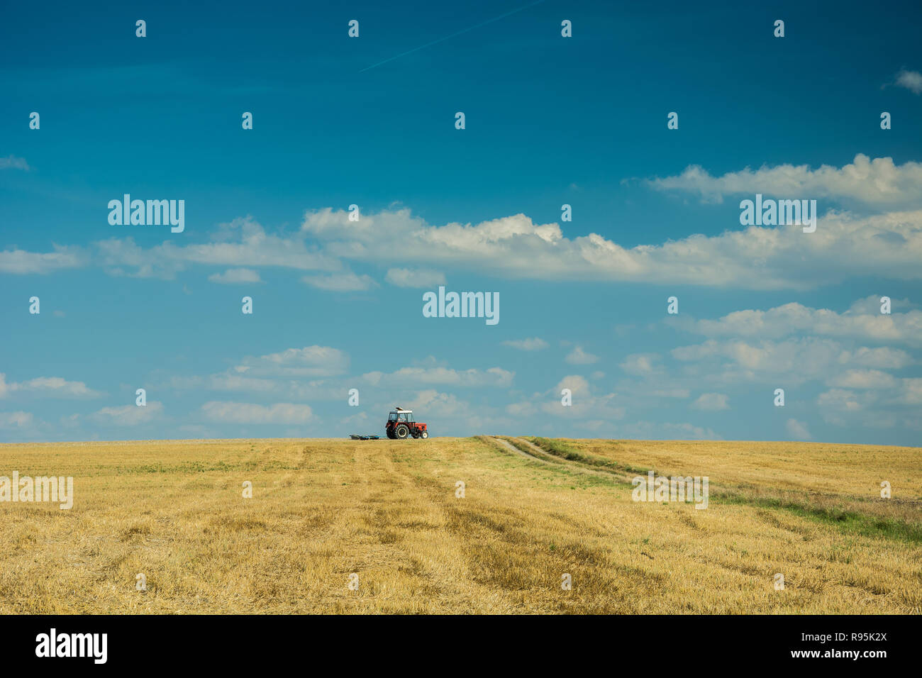 Conduite du tracteur sur chaume, d'horizon et les nuages sur le ciel bleu Banque D'Images