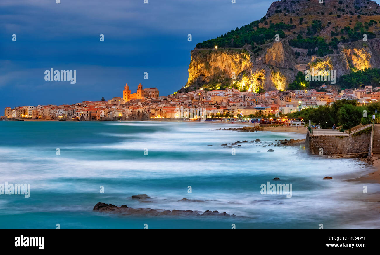 Blue Hour théâtre de la ville de Cefalù, avec la surface de la mer floue et allumé dans la montagne de l'île de la Sicile, Italie Banque D'Images