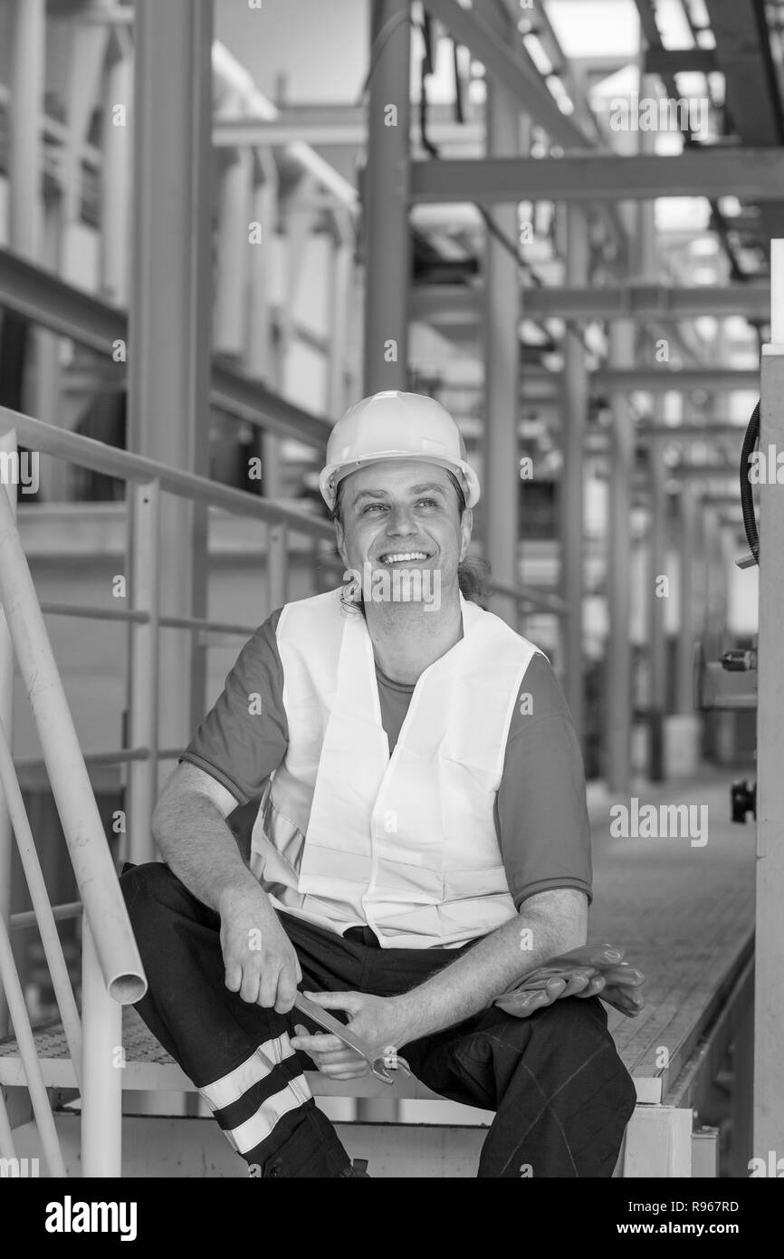 Image en noir et blanc de cheerful employé d'usine se reposant dans une usine et souriant Banque D'Images