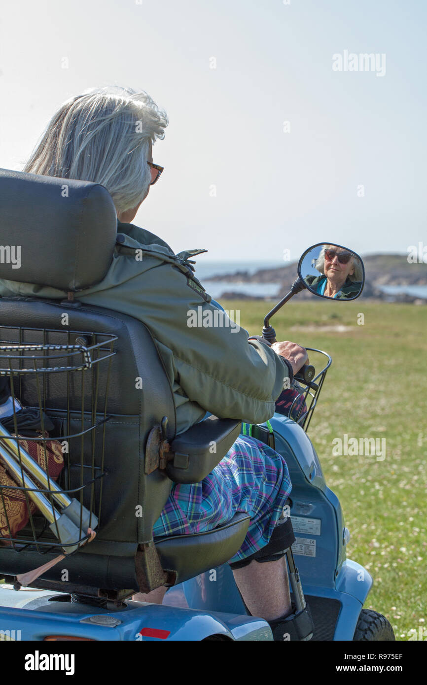 Mobilité. P​Hysically visuelle, PAO. Une femme âgée, de conduire un véhicule électrique à quatre roues agréable donnant l'indépendance et l'accès à l'​The campagne, milieu rural. Iona, côte ouest, l'Écosse. Banque D'Images