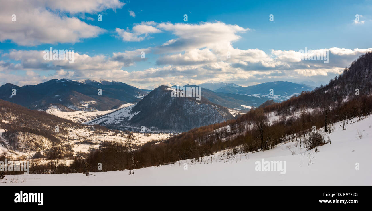 Panorama de la campagne d'hiver dans les montagnes. belle journée ensoleillée avec de magnifiques nuages. forêt sombre sur les collines couvertes de neige dans le village. Banque D'Images