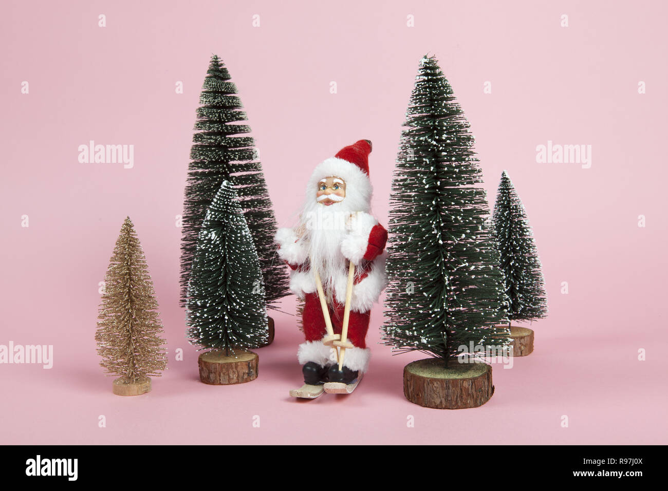 Un Santa Claus figurine ski entre les sapins miniatures sur fond rose. L'harmonie des couleurs. Un minimum de vie encore la photographie en couleurs Banque D'Images