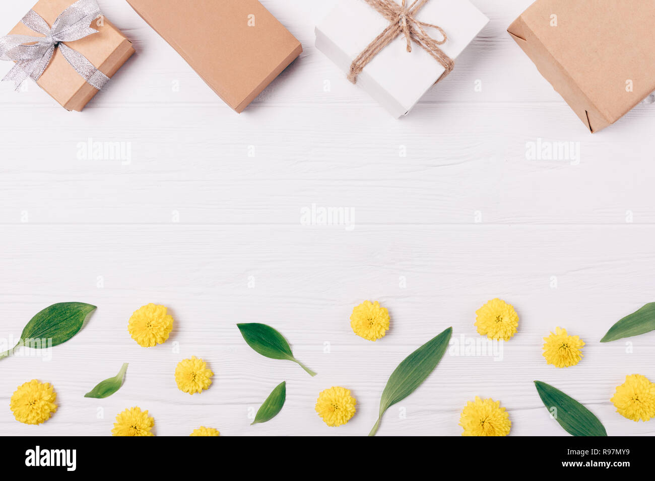 Vue de dessus cadre décoratif fait de coffrets cadeaux sur feuilles vertes et jaunes des boutons de fleurs sur fond de bois blanc, télévision jeter la composition avec fre Banque D'Images