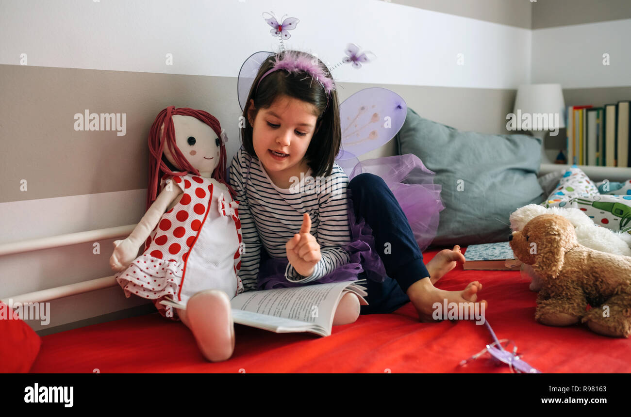 Déguisée de fille lire un livre à sa poupée Banque D'Images