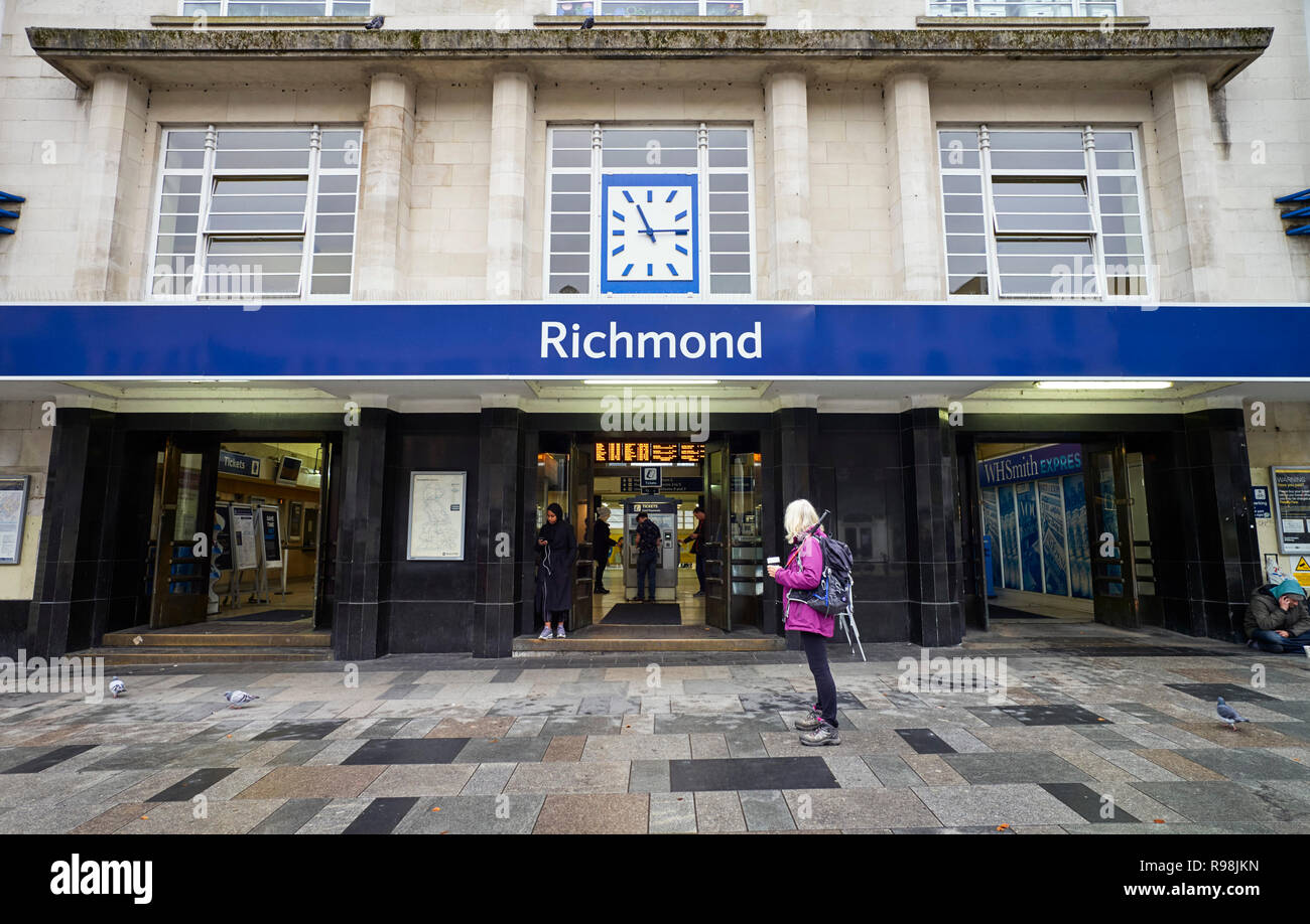 Une femme avec un pôle de marche, bottes de randonnée et un sac à dos tenant une tasse de café à l'extérieur de la façade de style années 30 de la gare de Richmond sur la Tamise Banque D'Images