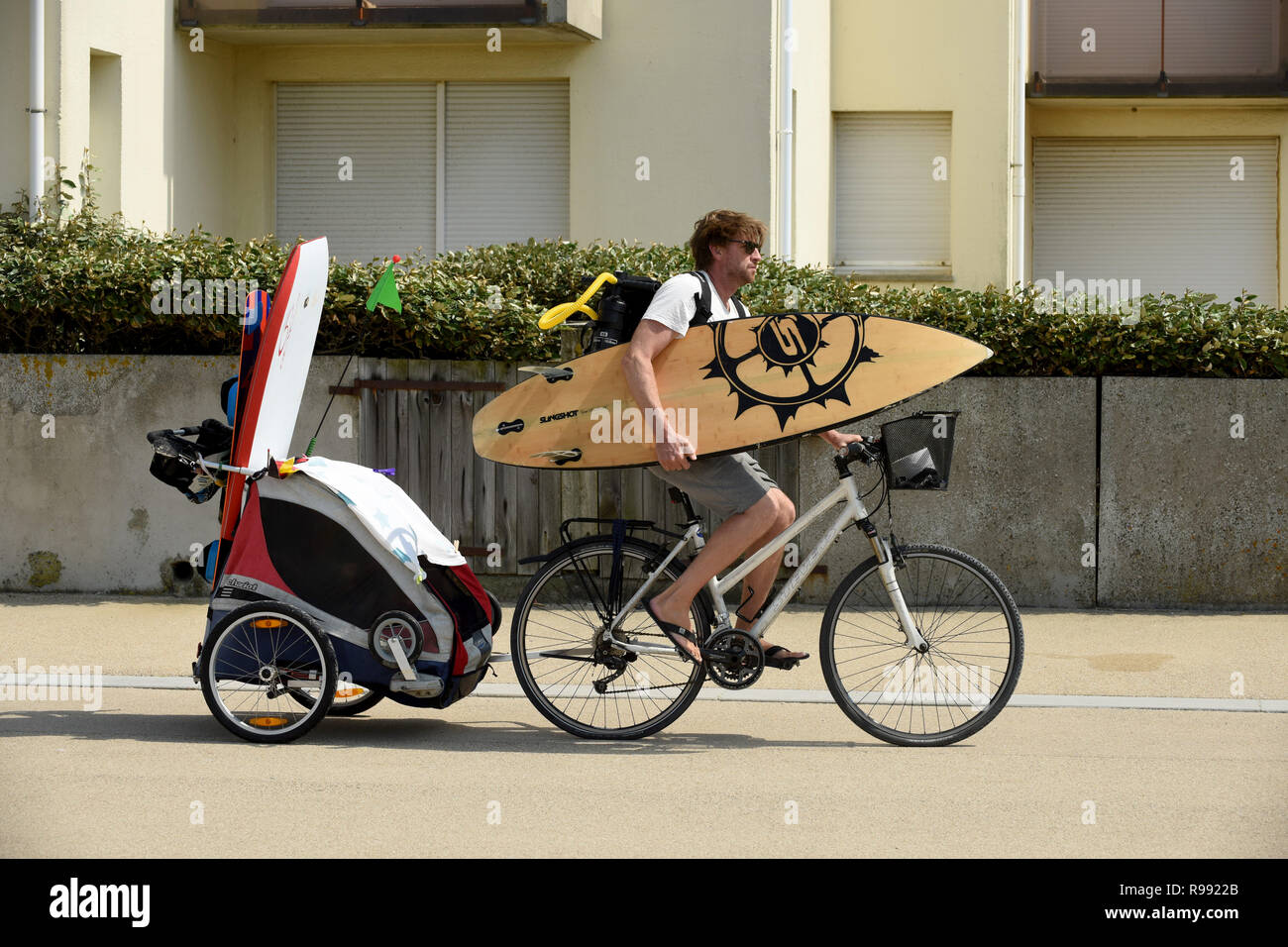 Surfer riding bike avec planche de surf et de remorquage remorque enfant à Wissant dans le nord de la France Banque D'Images