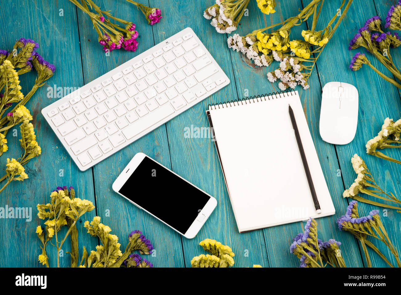 Lieu de travail avec slim sans fil clavier, souris, téléphone intelligent, le bloc-notes, des fleurs colorées sur un bureau en bois bleu Banque D'Images