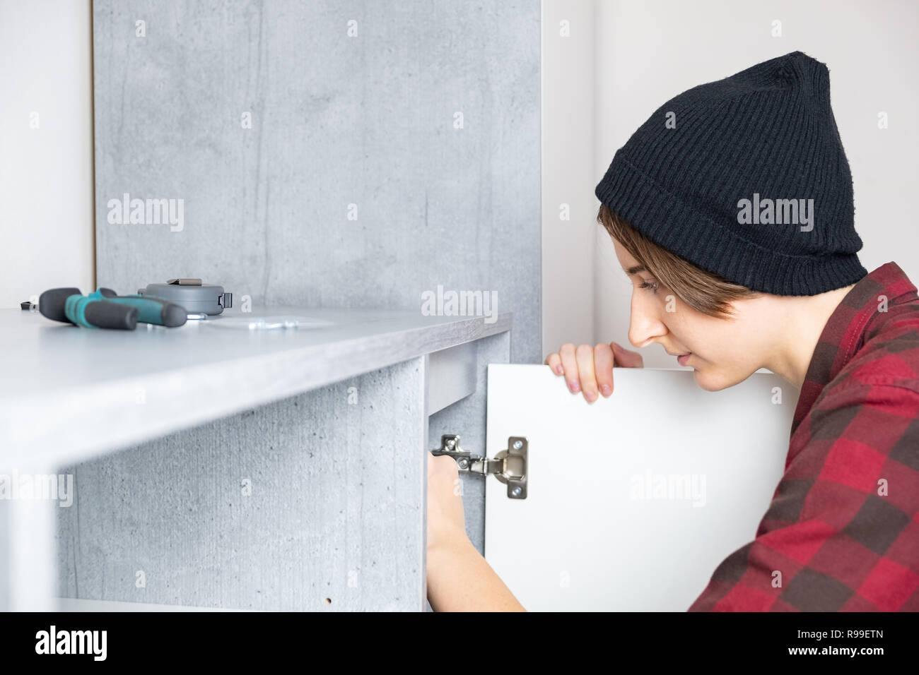 Réglage de la femme porte des meubles à la maison. Femme en chemise décontractée et Knit hat ne hommes stéréotypées. Banque D'Images