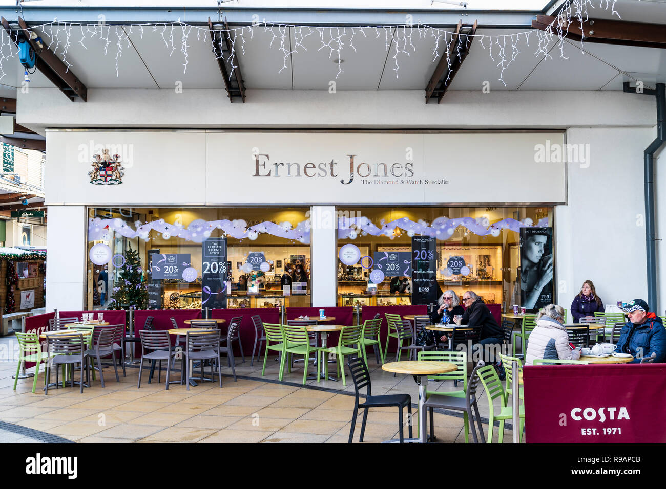 Super Samedi, le dernier week-end avant Noël au centre commercial Westwood Cross. Ernest Jones bijoutiers avec signes fenêtre offrant 20 % de rabais. En premier plan cinq personnes assises sur coin salon extérieur. Banque D'Images