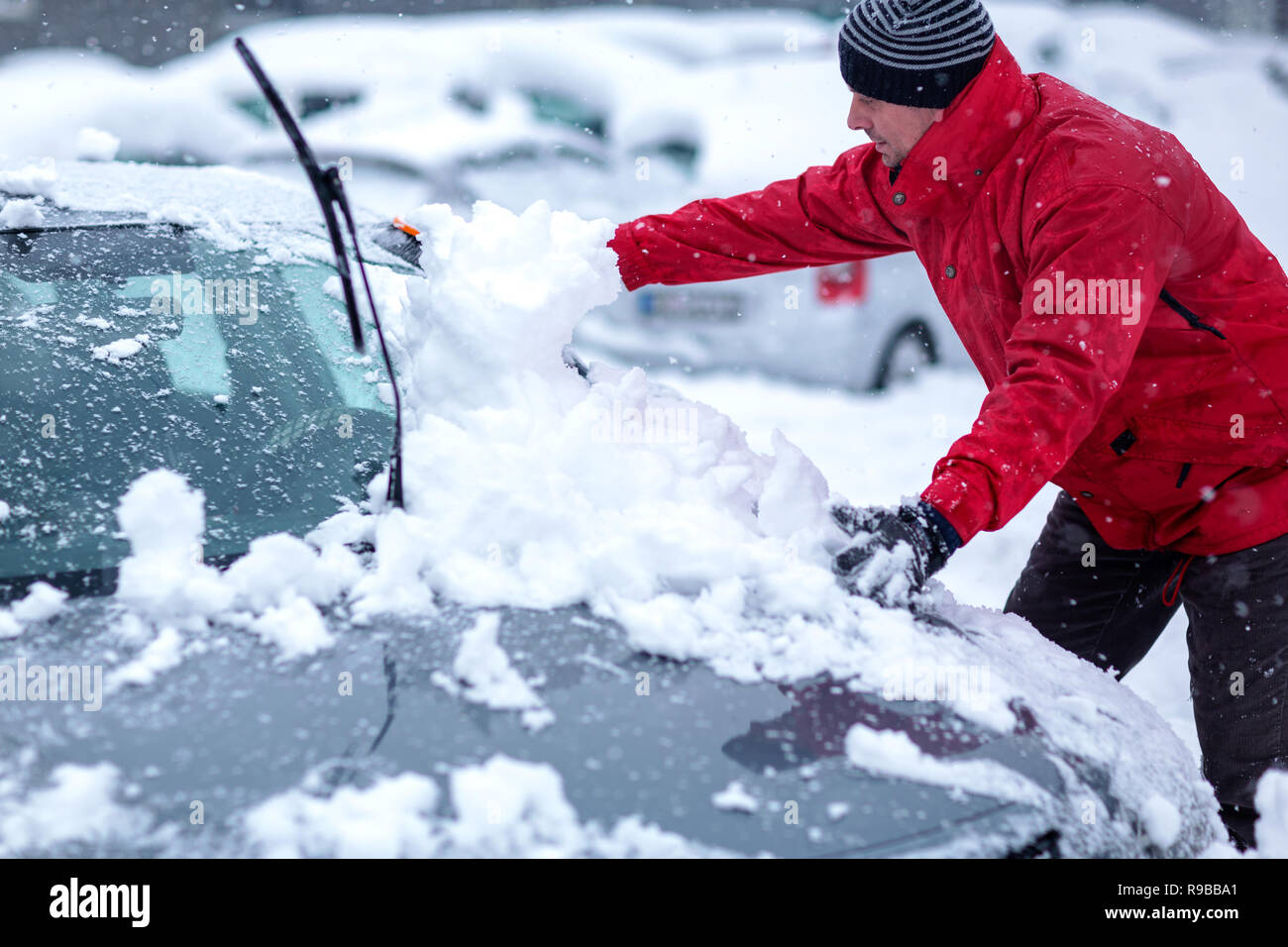 Problèmes d'hiver des automobilistes. Un homme se brosser la neige de la voiture. Jeune homme l'enlèvement de la neige à partir de la voiture. Banque D'Images