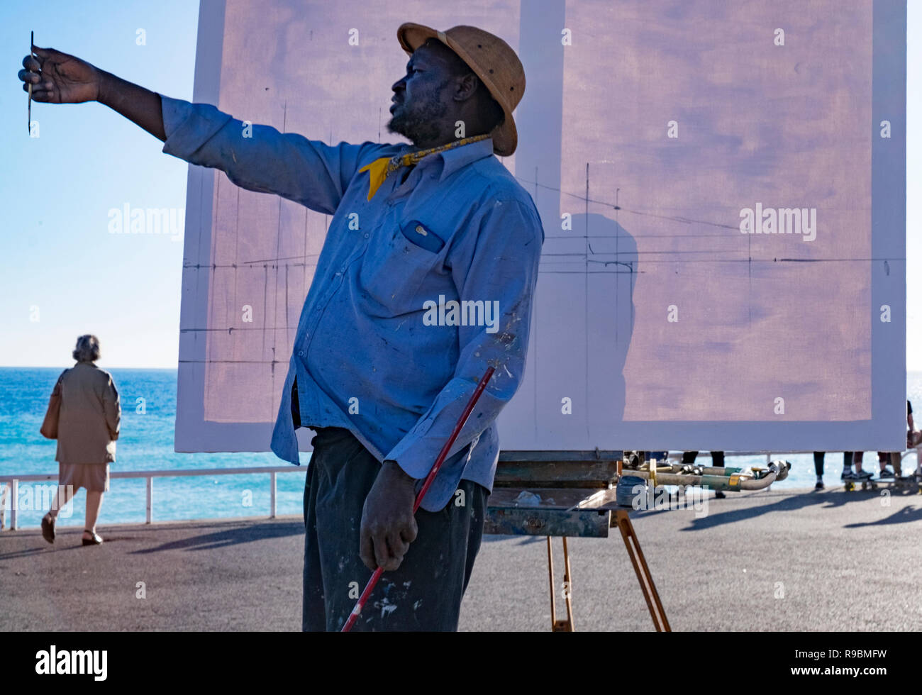 Artiste noir dans safari hat installe son chevalet pour peindre une scène en plein air avec ses pinceaux et toiles. Banque D'Images