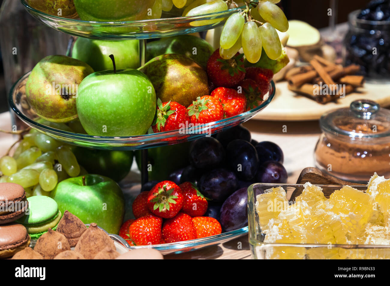 Fruits frais lumineux Gros plan : pommes, poires, fraises, raisins, miel cubes dans un bol en verre, fleurs d'iris, macarons, truffes sur table du buffet. Con Banque D'Images